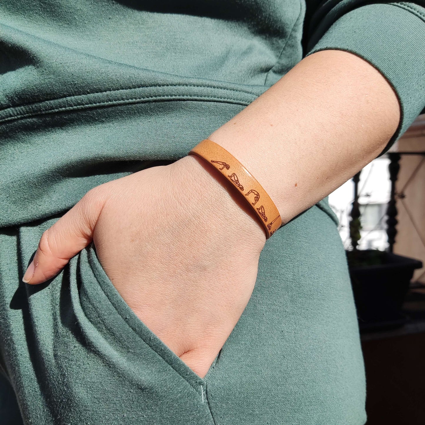 A brown leather bracelet with a bridge yoga flow engraved on it.