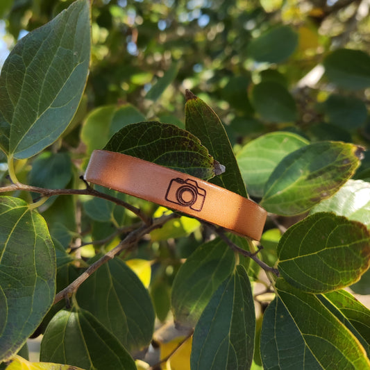 A brown leather bracelet with a camera engraved on it.