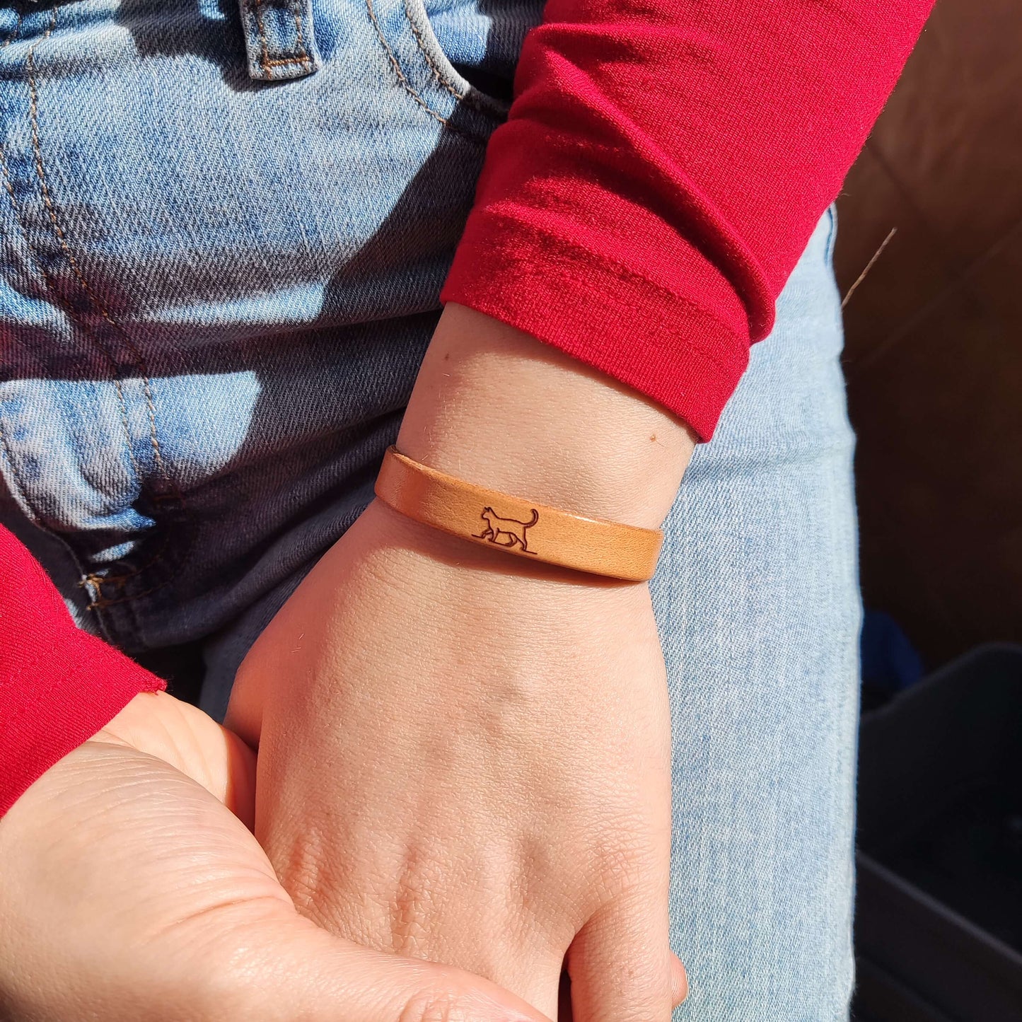 A brown leather bracelet with a cat engraved on it.