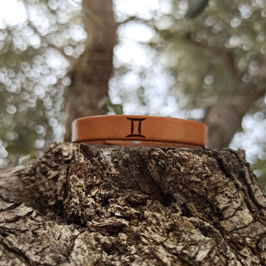 A brown leather bracelet with gemini´s symbol engraved on it.