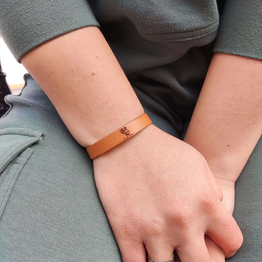 A brown leather bracelet with a koala engraved on it.