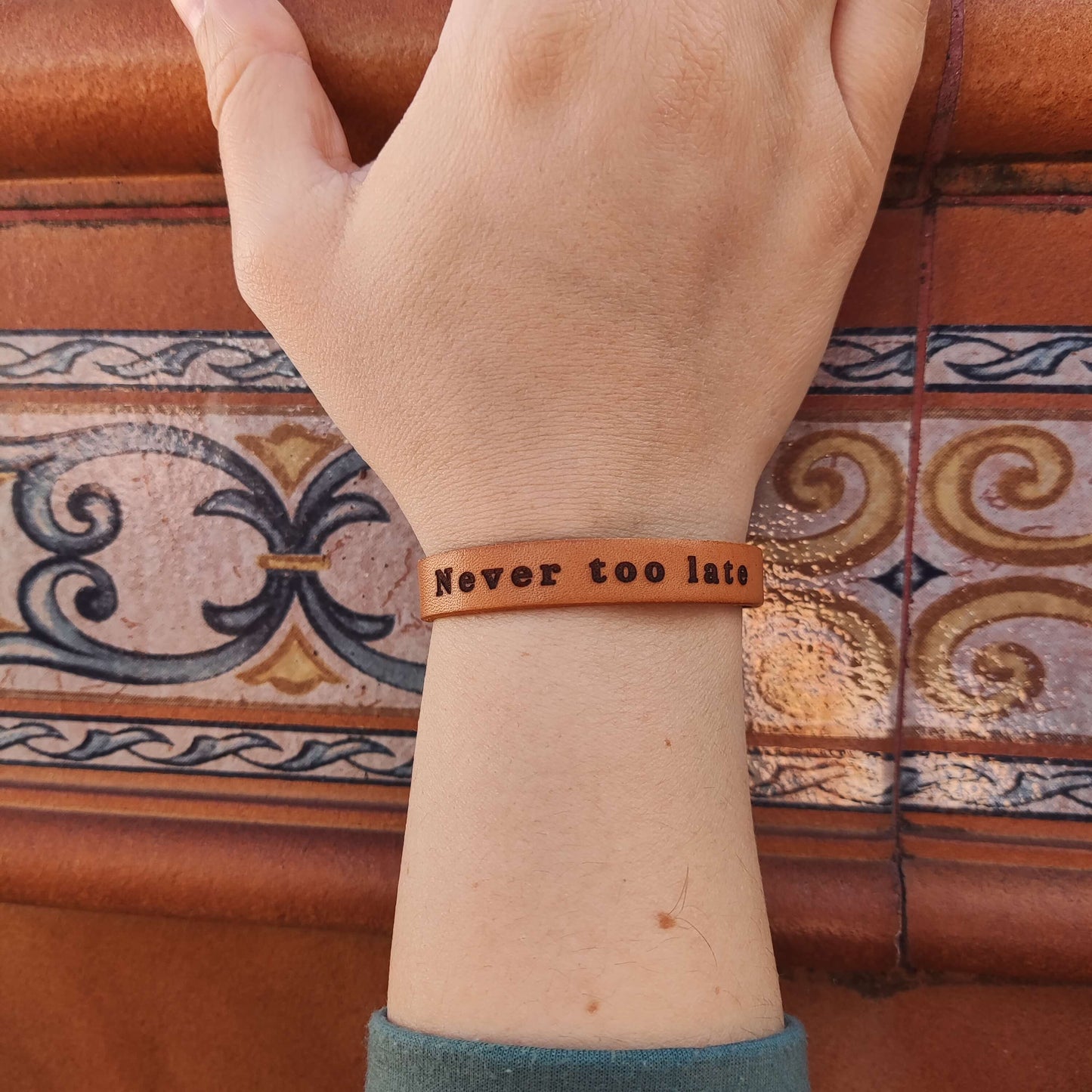 A brown leather bracelet with the phrase `Never too late´ engraved on it.