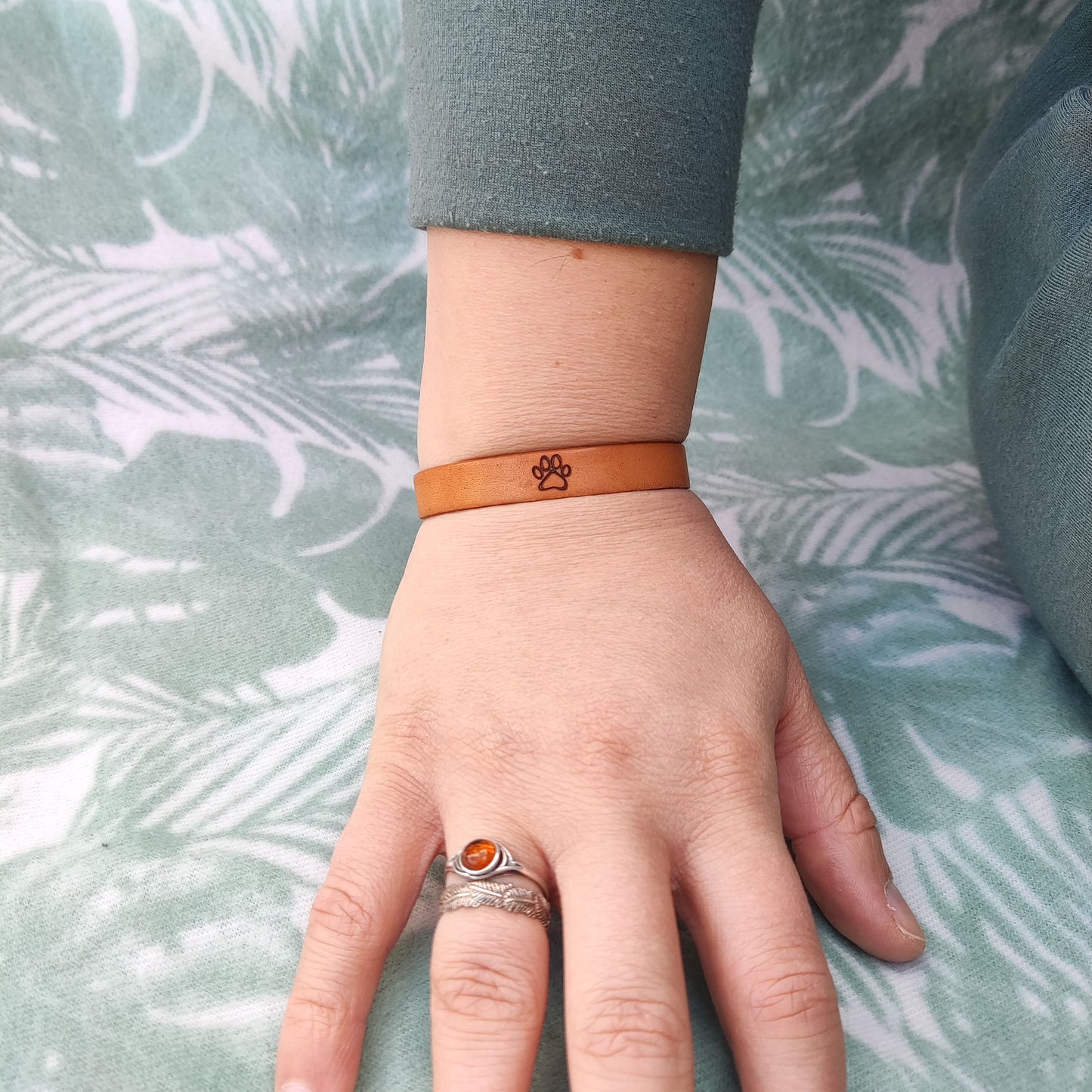 A brown leather bracelet with a paw print engraved on it.