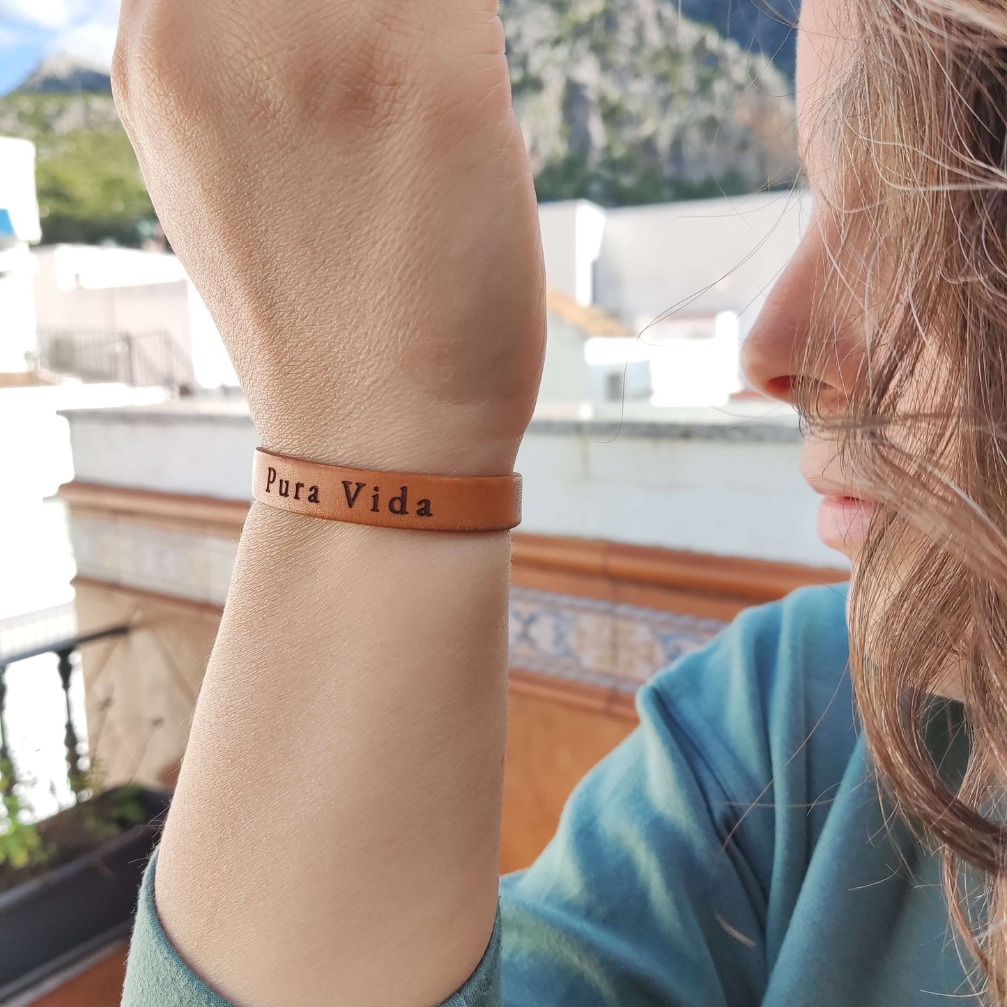 A brown leather bracelet with 'Pura Vida' engraved on it.