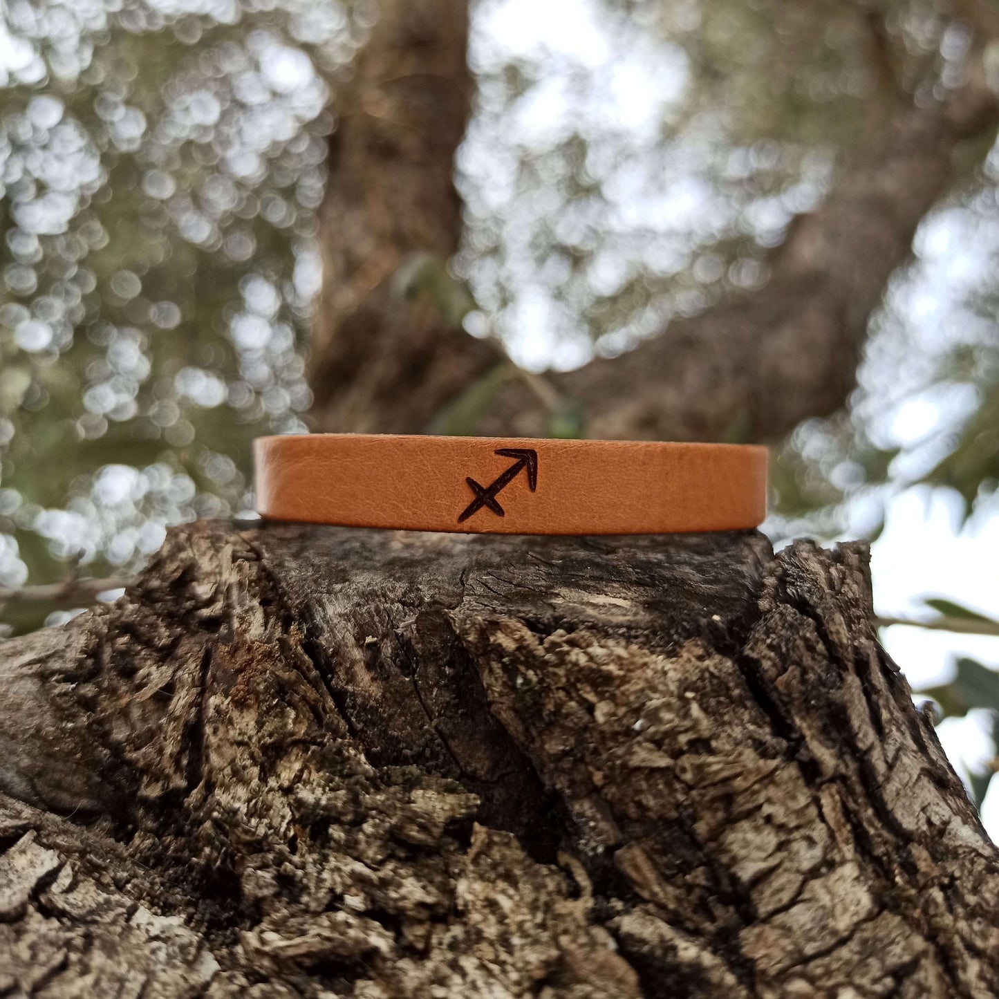 A brown leather bracelet with sagitarrius´ horoscope symbol engraved on it.