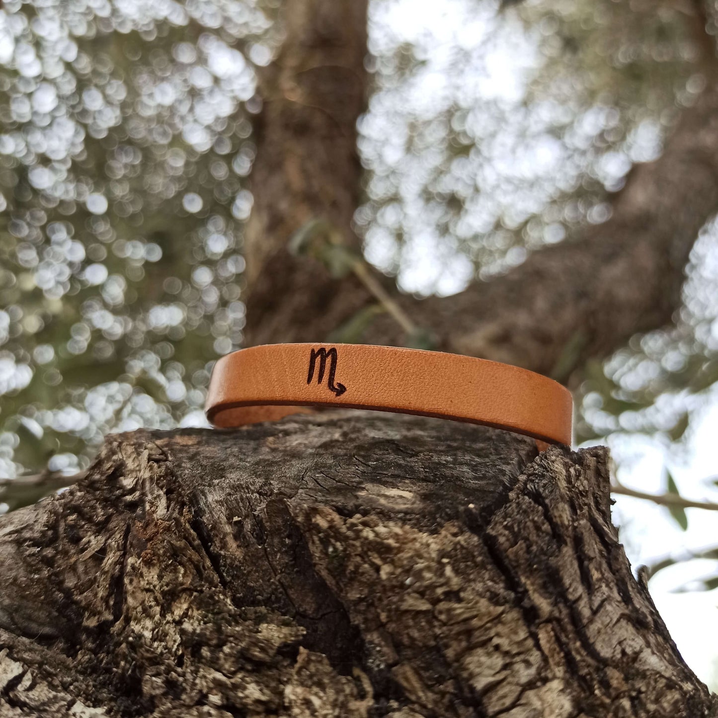 A brown leather bracelet with scorpio´s symbol engraved on it.