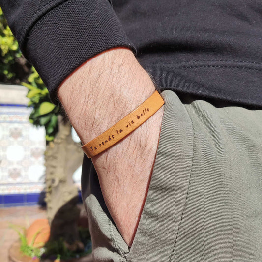 A brown leather bracelet with `Tu rends la vie belle´ engraved on it.