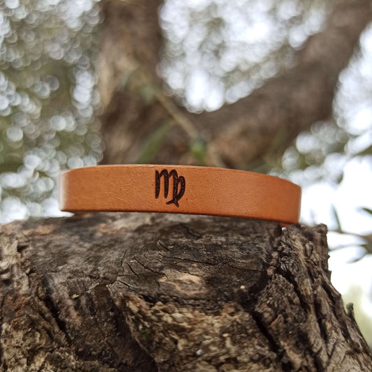 A brown leather bracelet with virgo´s symbol engraved on it.