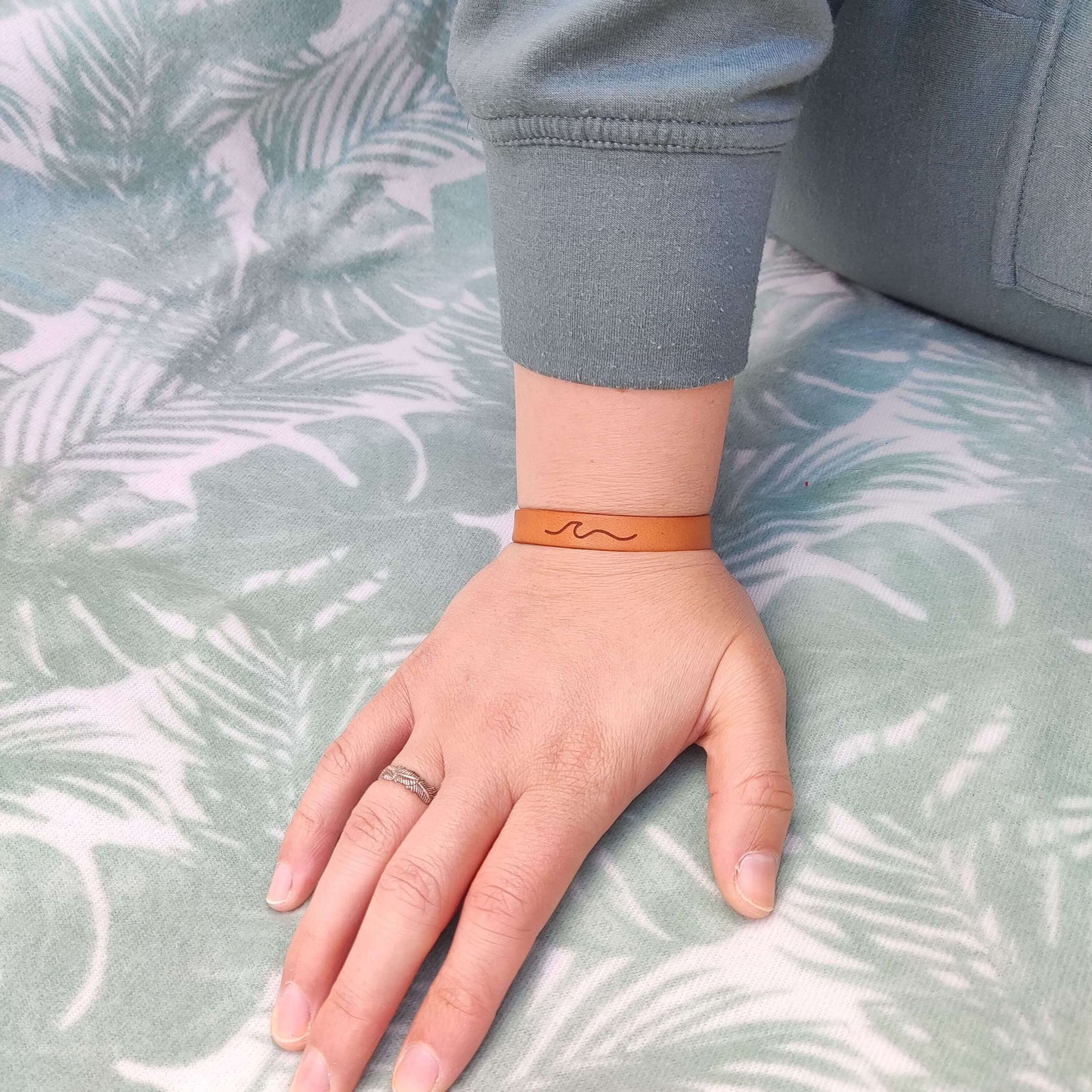 A brown leather bracelet with a wave engraved on it.
