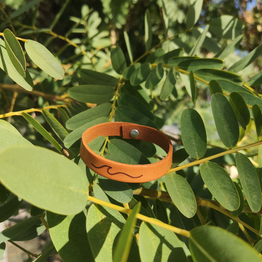 A brown leather bracelet with a wave engraved on it.