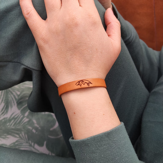 A brown leather bracelet with the world engraved on it.
