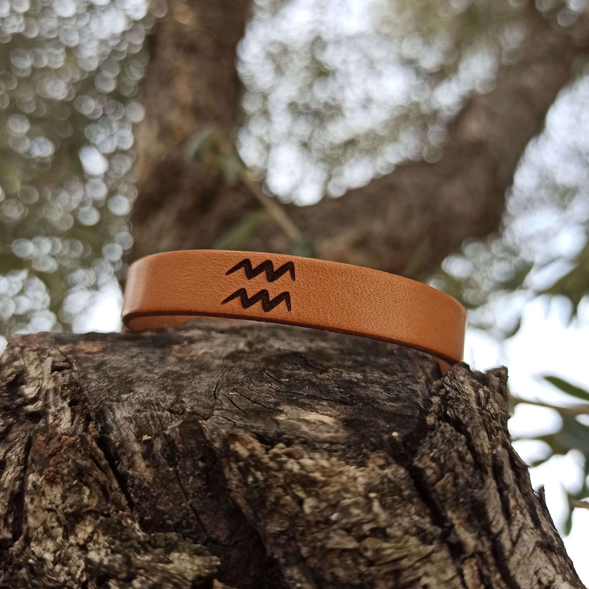 A brown leather bracelet with Aquarius´ symbol engraved on it.