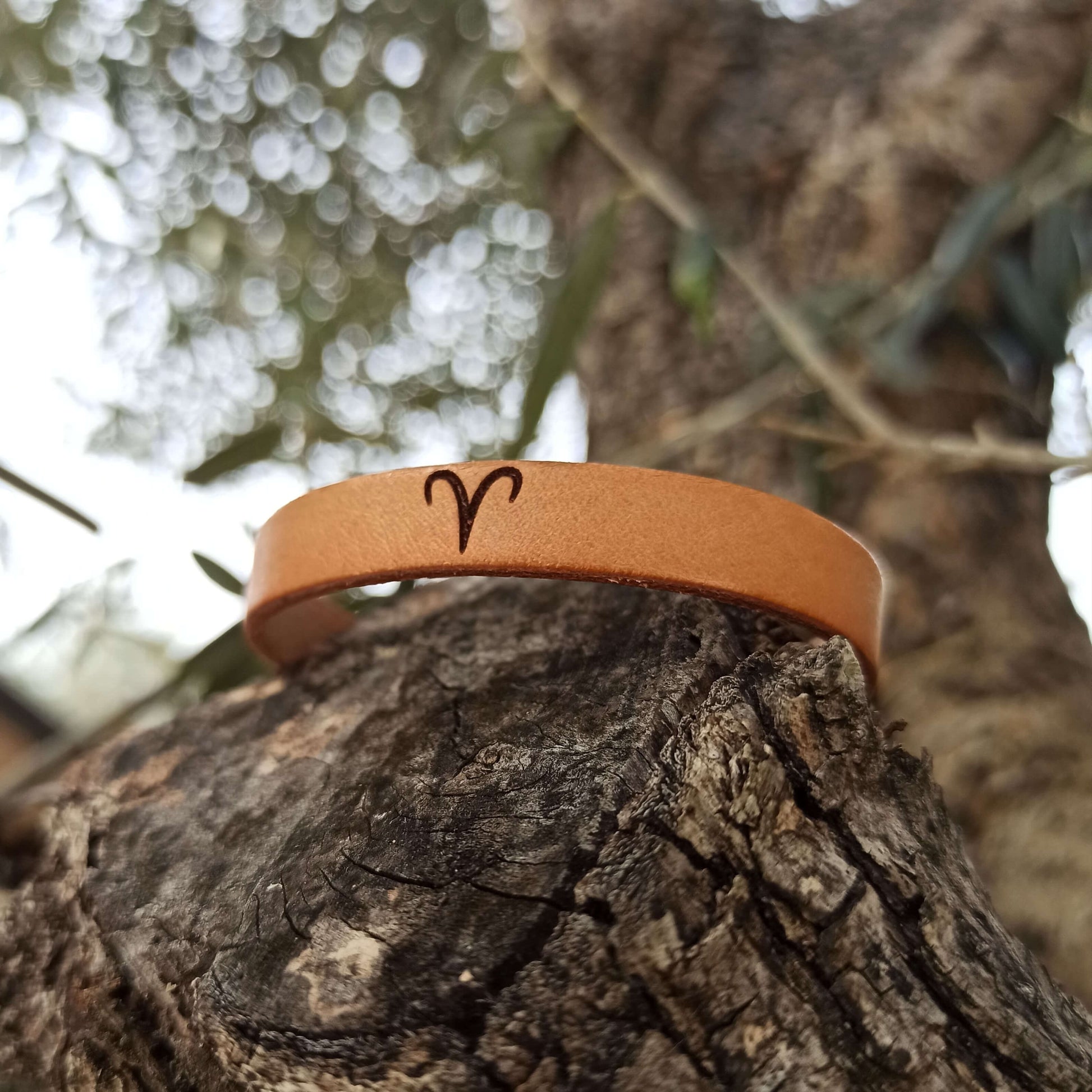 A brown leather bracelet with aries´ symbol engraved on it.