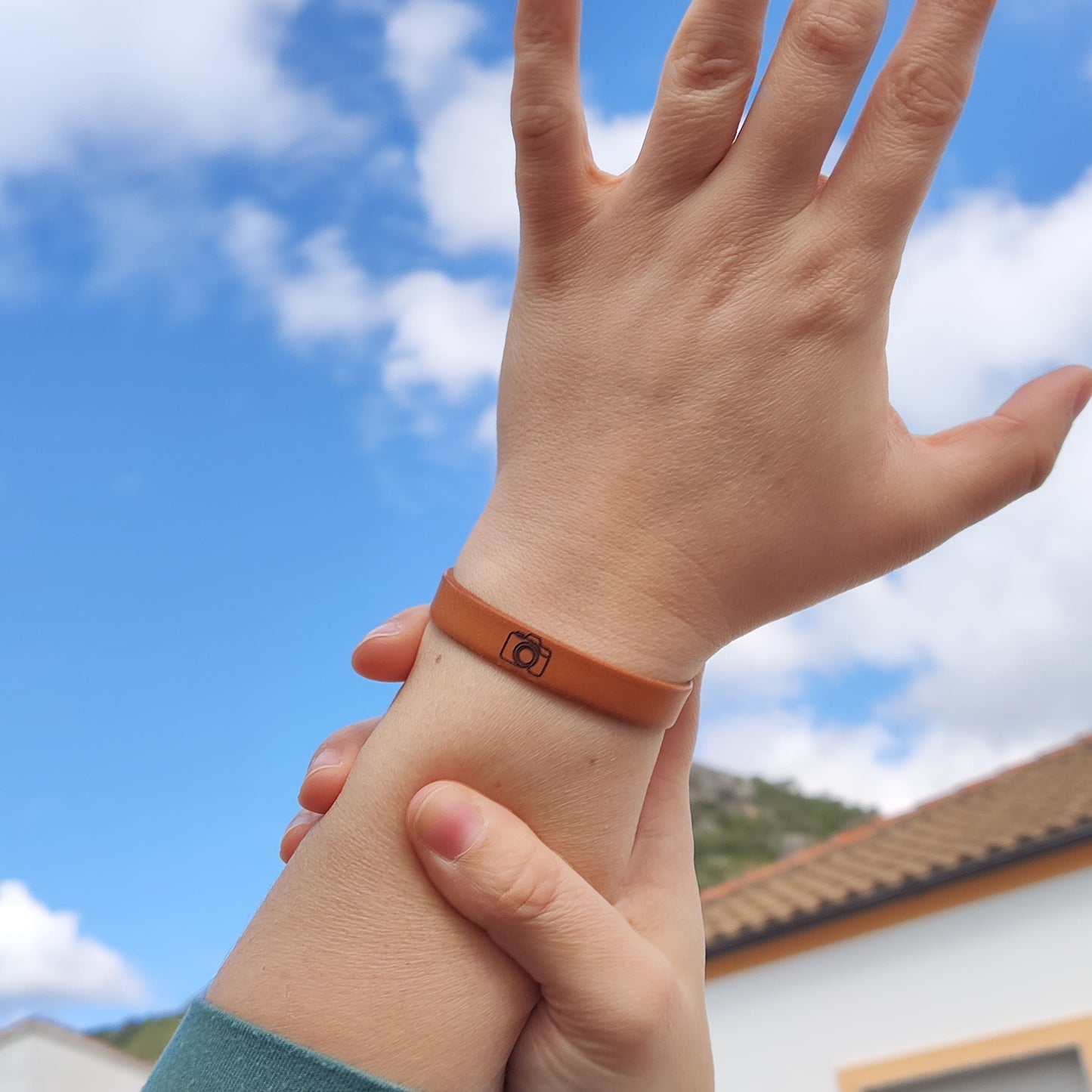 A brown leather bracelet with a camera engraved on it.