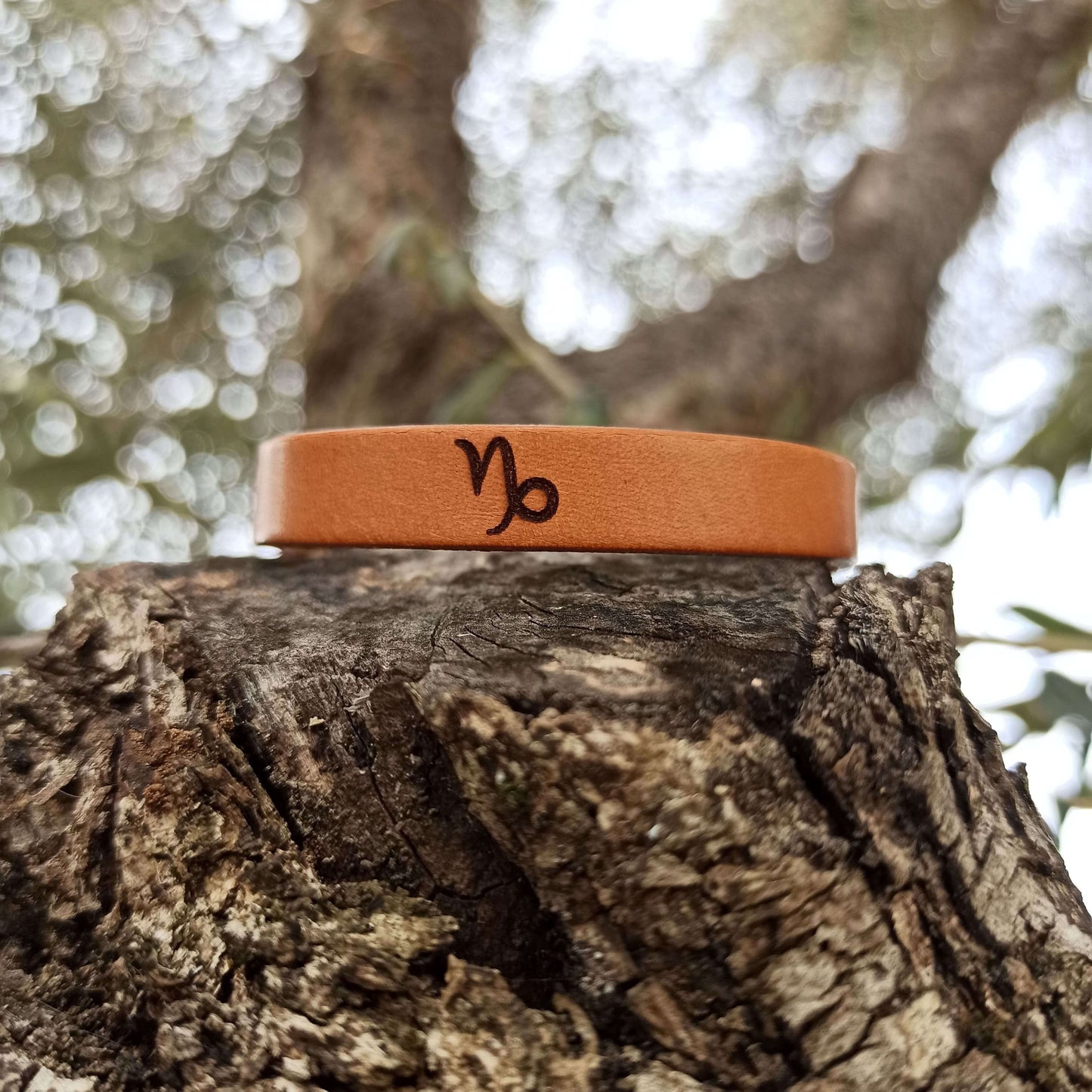 A brown leather bracelet with capricorn´s symbol engraved on it.
