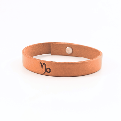 A brown leather bracelet with capricorn´s symbol engraved on it.