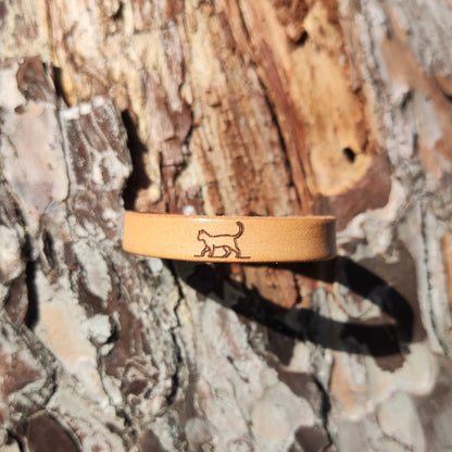 A brown leather bracelet with a cat engraved on it.