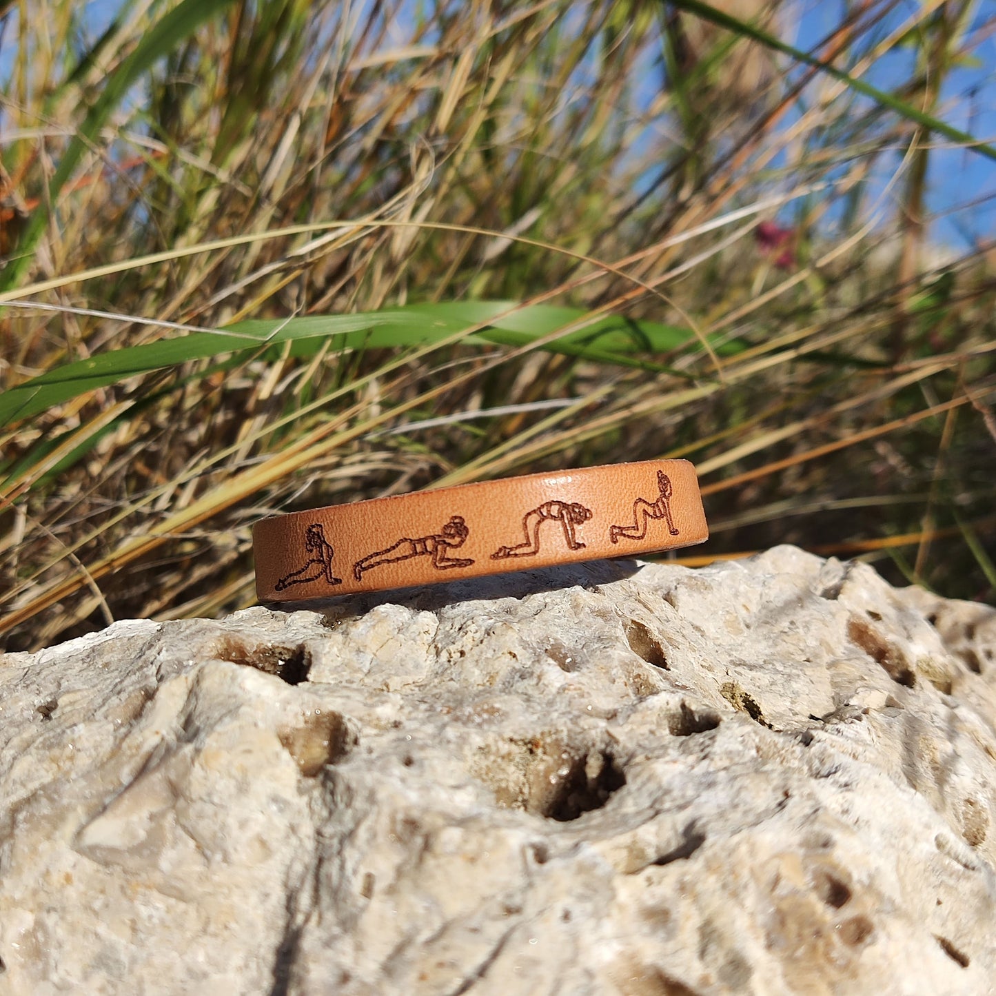A brown leather bracelet with a cat cow yoga flow engraved on it.