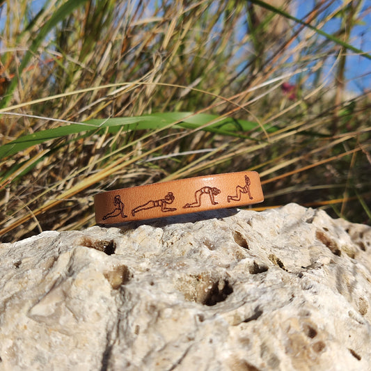 A brown leather bracelet with a cat cow yoga flow engraved on it.