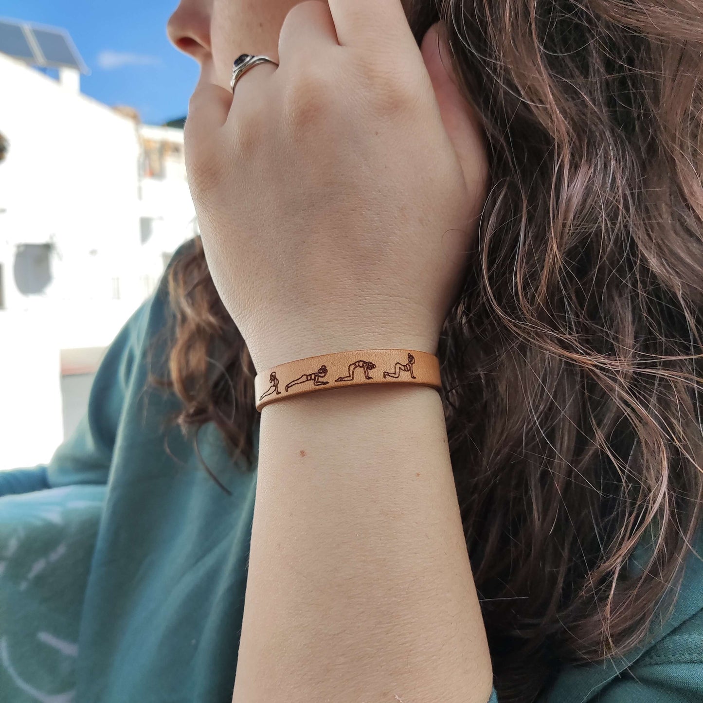 A brown leather bracelet with a cat cow yoga flow engraved on it.