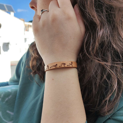 A brown leather bracelet with a cat cow yoga flow engraved on it.