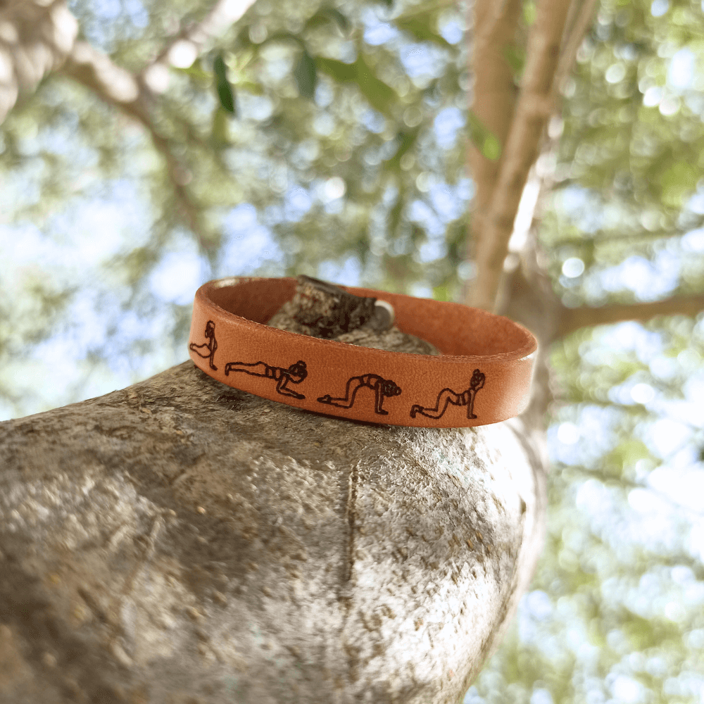 A brown leather bracelet with a cat cow yoga flow engraved on it.