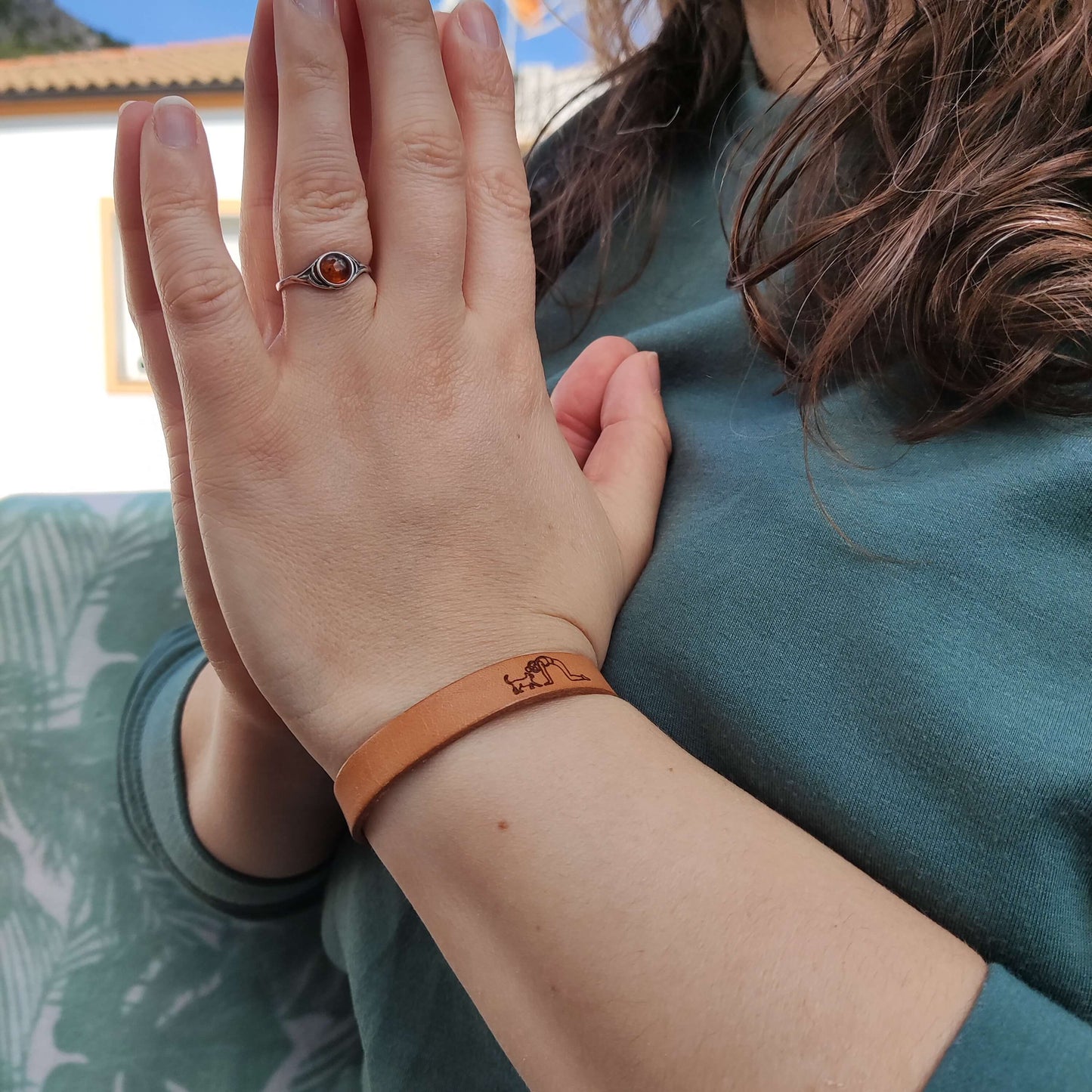 A brown leather bracelet with a cat and lady doing yoga engraved on it.