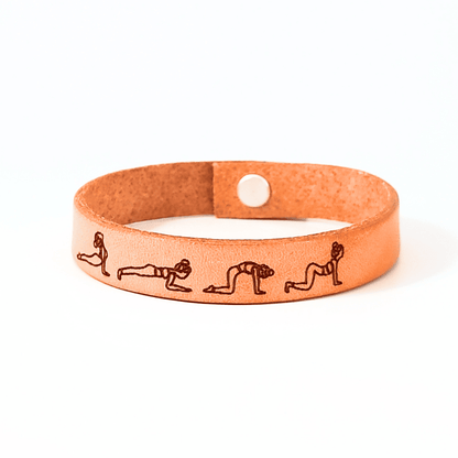 A brown leather bracelet with cat - cow yoga flow engraved on it.