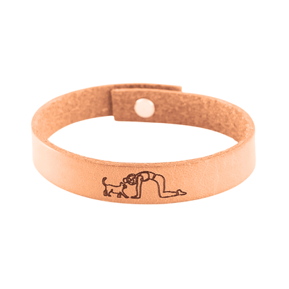 A brown leather bracelet with a cat and lady doing yoga engraved on it.
