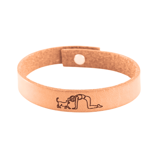 A brown leather bracelet with a cat and lady doing yoga engraved on it.