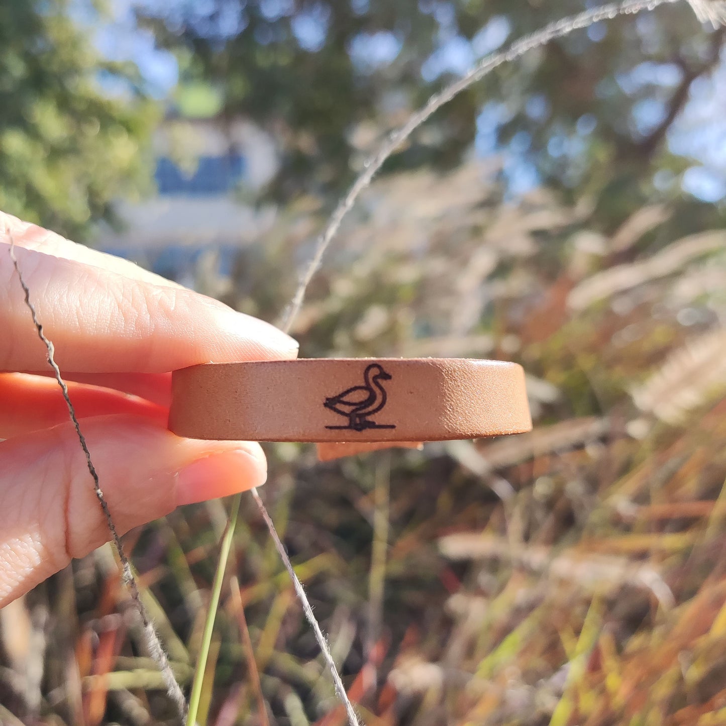 A brown leather bracelet with a duck engraved on it.