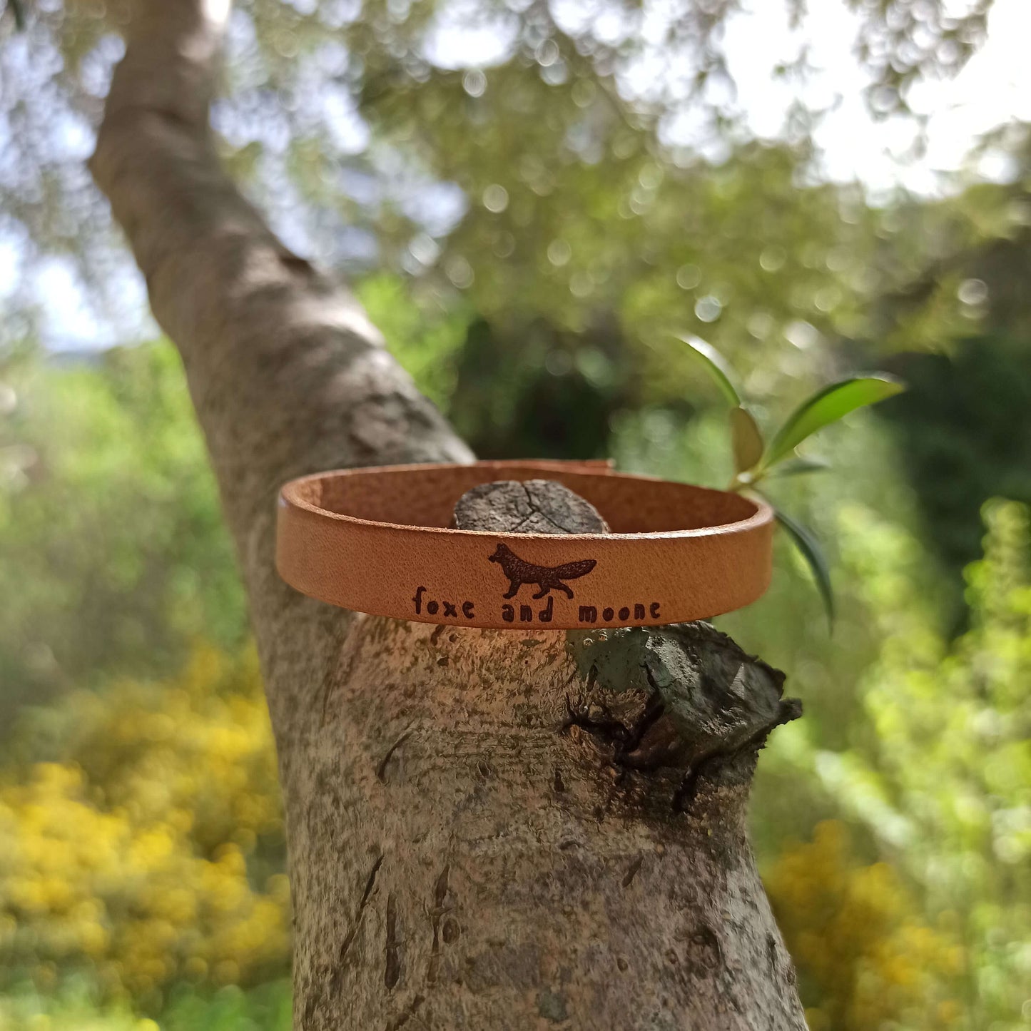A brown leather bracelet with an image of a fox and the text 'Foxe and Moone.' engraved on it.