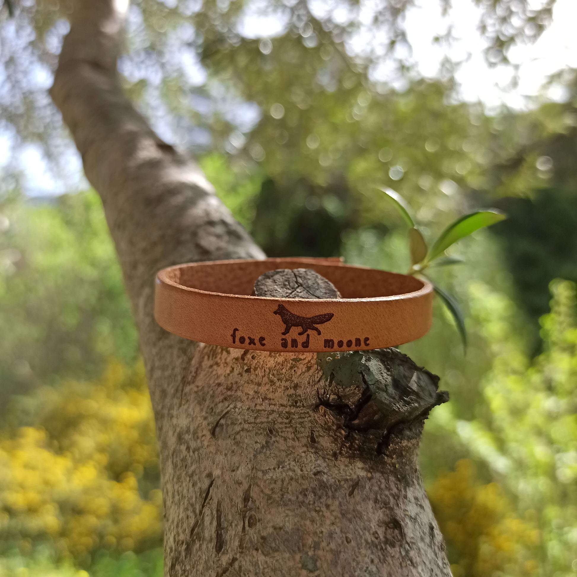A brown leather bracelet with an image of a fox and the text 'Foxe and Moone.' engraved on it.