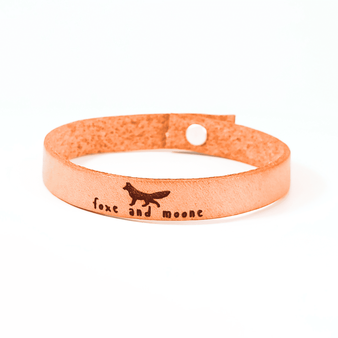 A brown leather bracelet with an image of a fox and the text 'Foxe and Moone.' engraved on it.