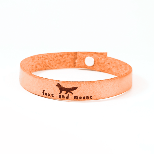 A brown leather bracelet with an image of a fox and the text 'Foxe and Moone.' engraved on it.