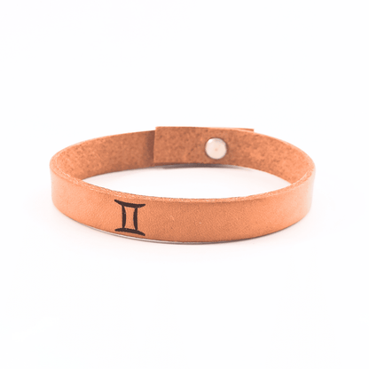 A brown leather bracelet with gemini´s symbol engraved on it.