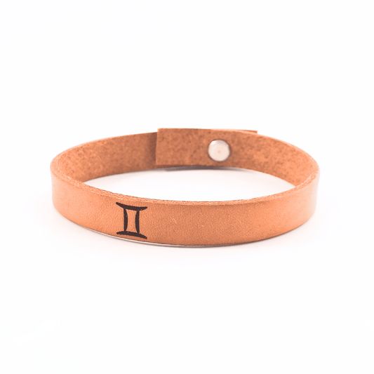 A brown leather bracelet with gemini´s symbol engraved on it.