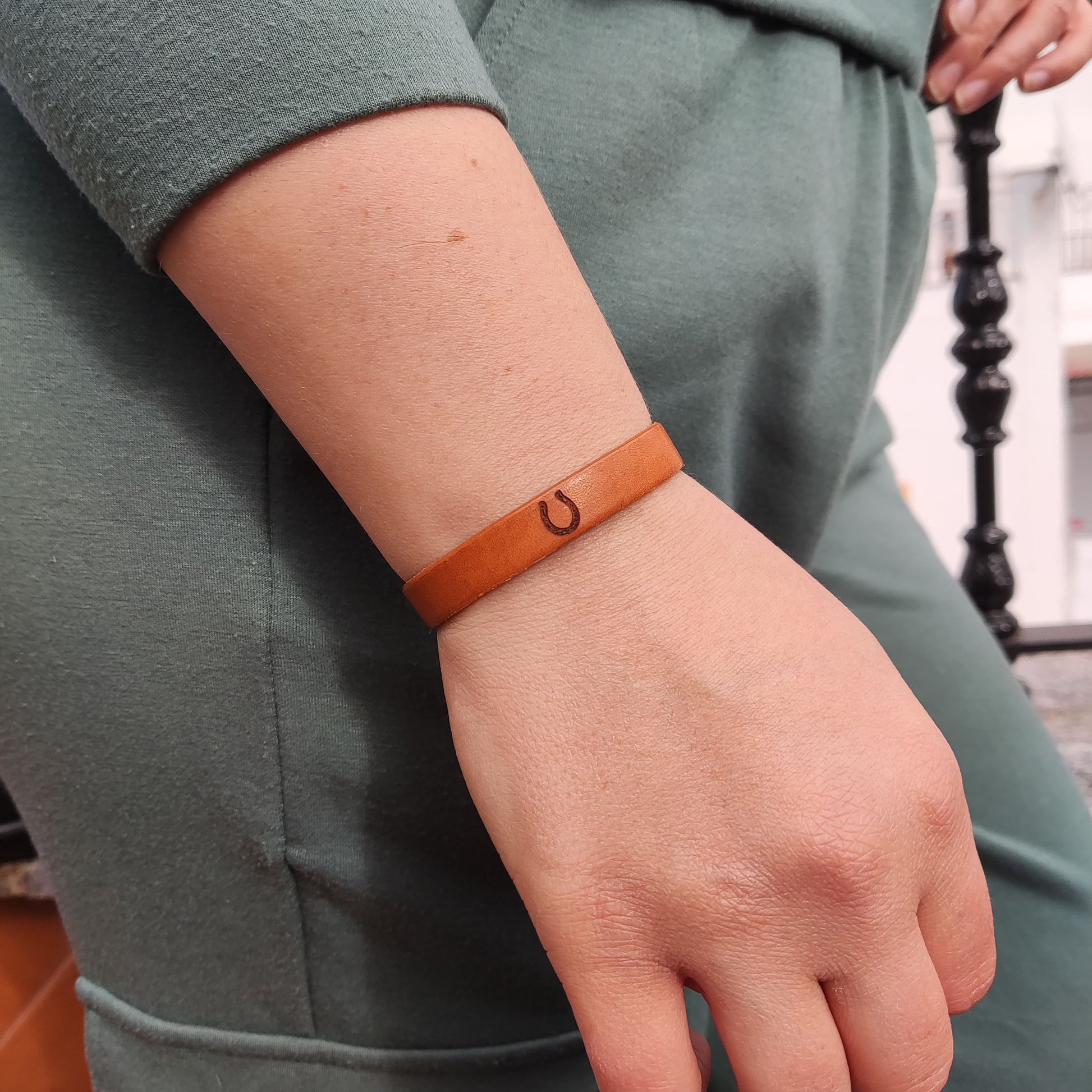 A brown leather bracelet with a horseshoe engraved on it.
