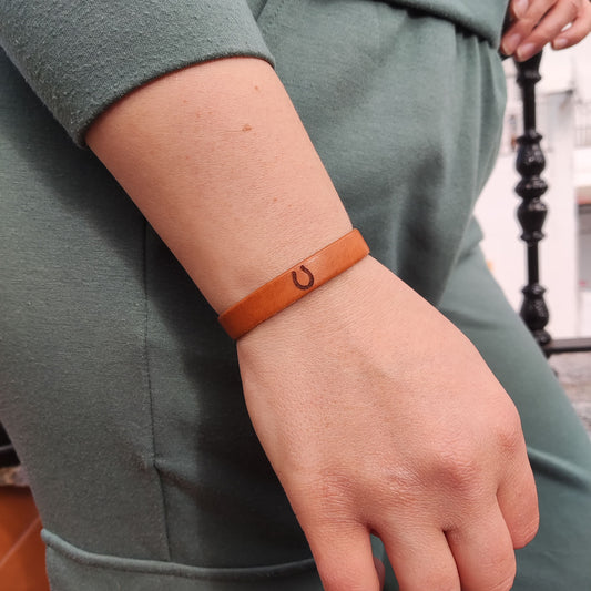 A brown leather bracelet with a horseshoe engraved on it.