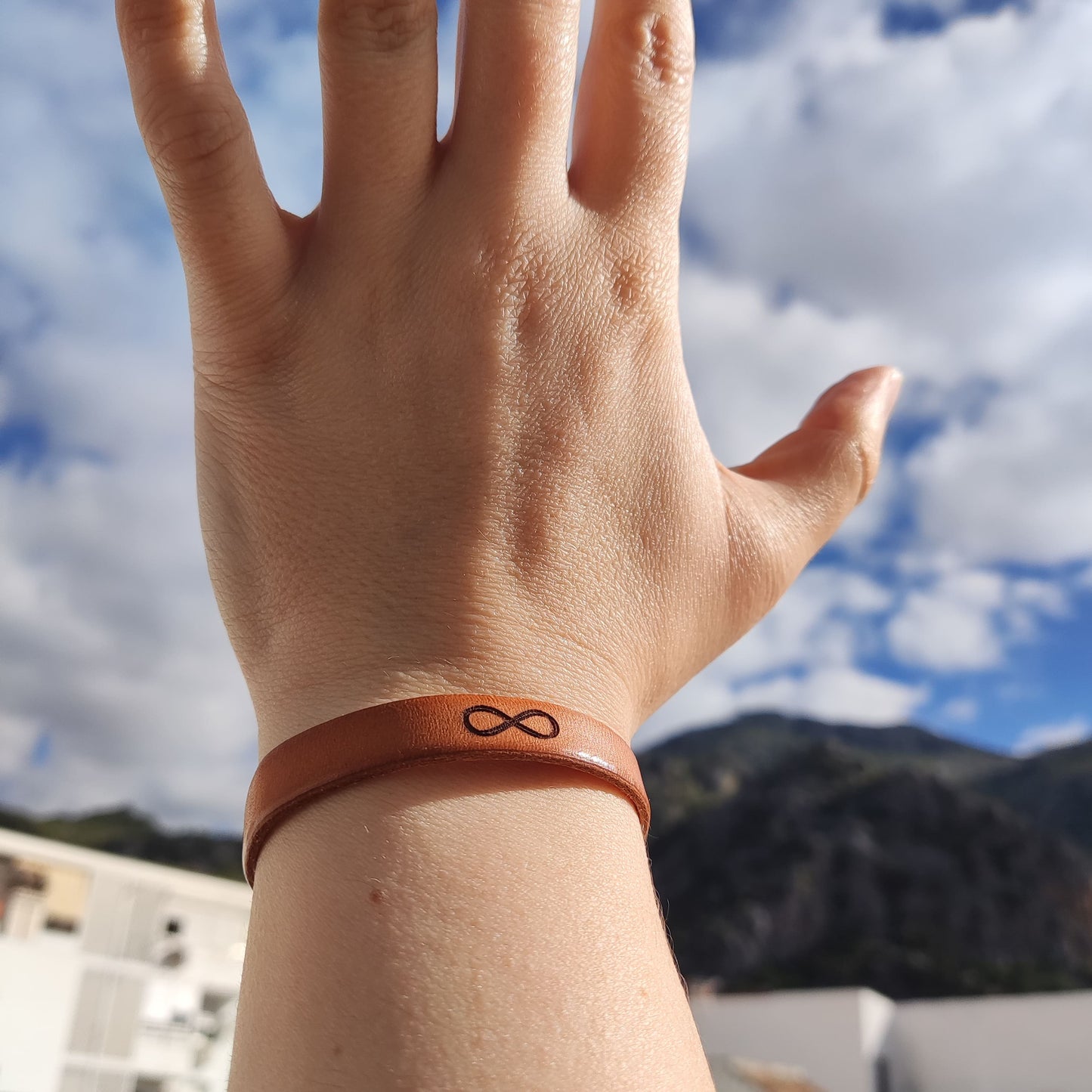 A brown leather bracelet with an infinity symbol engraved on it.