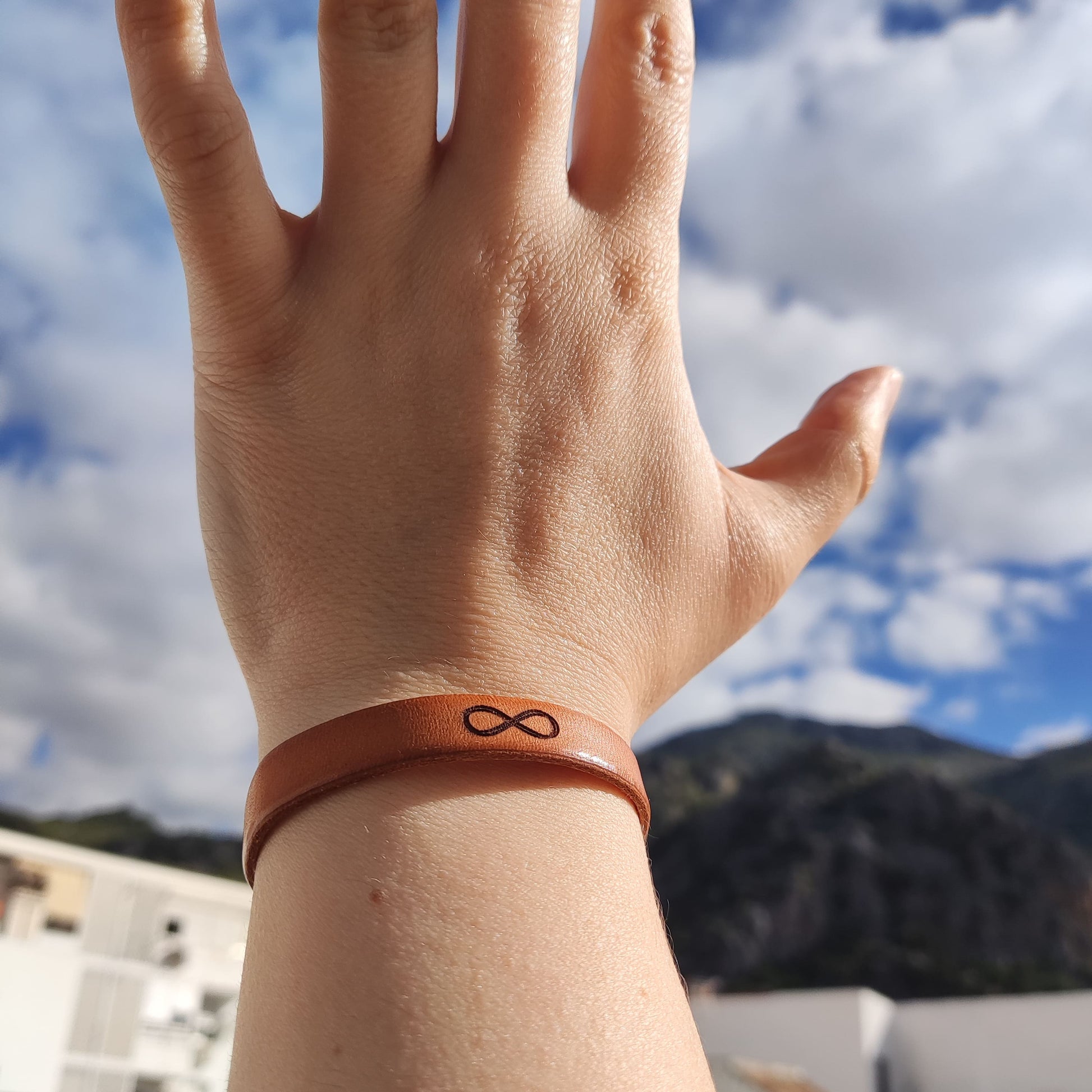 A brown leather bracelet with an infinity symbol engraved on it.