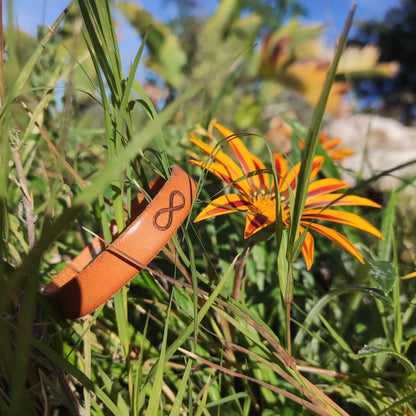 A brown leather bracelet with an infinity symbol engraved on it.