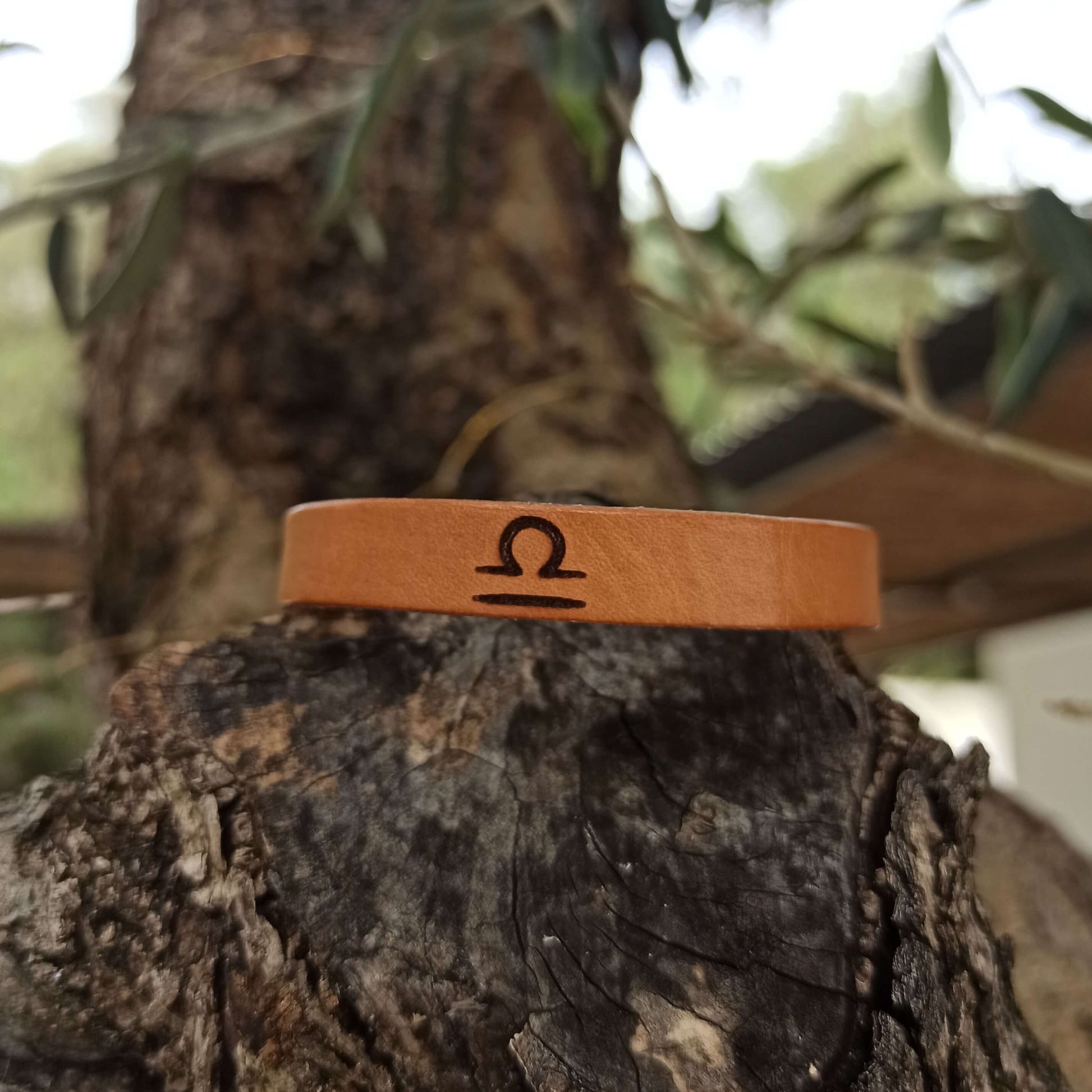 A brown leather bracelet with libra´s symbol engraved on it.