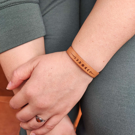 A brown leather bracelet with the lunar phases engraved on it.