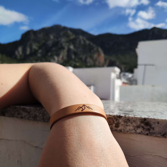 A brown leather bracelet with the mountains engraved on it.