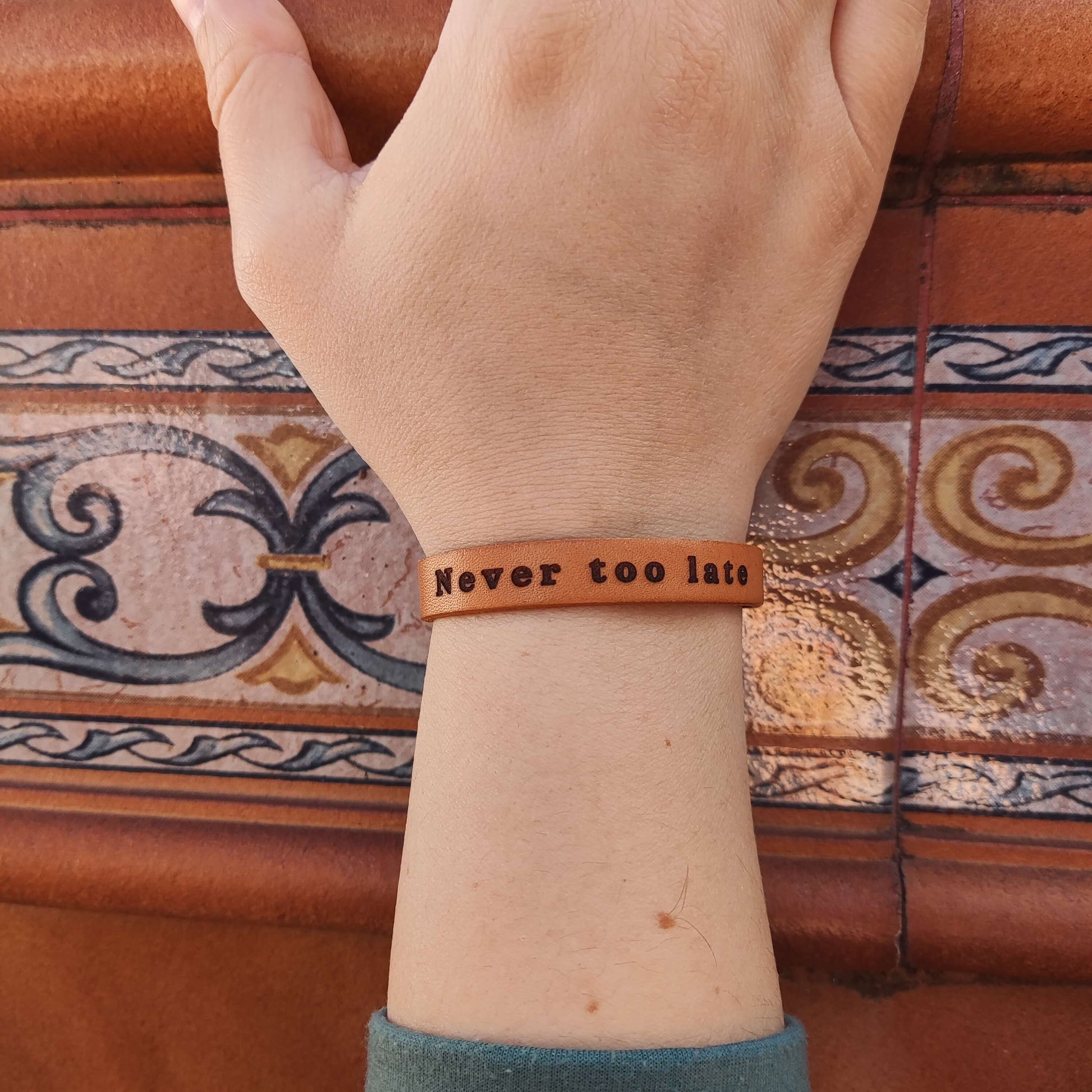 A brown leather bracelet with the phrase `Never too late´ engraved on it.