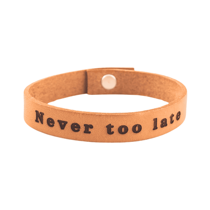 A brown leather bracelet with the phrase `Never too late´ engraved on it.