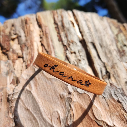 A brown leather bracelet with the phrase `Ohana´ engraved on it.