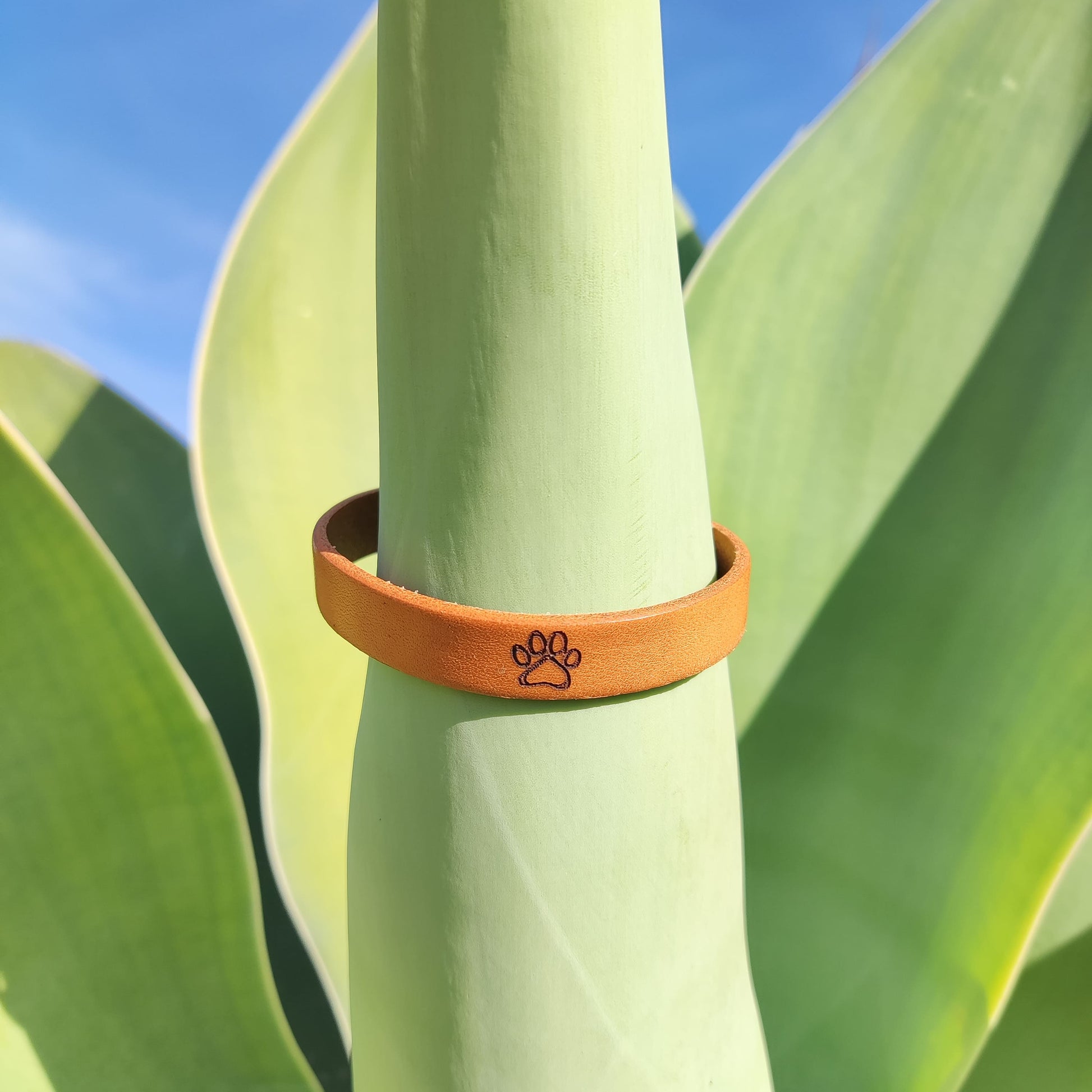A brown leather bracelet with a paw print engraved on it.