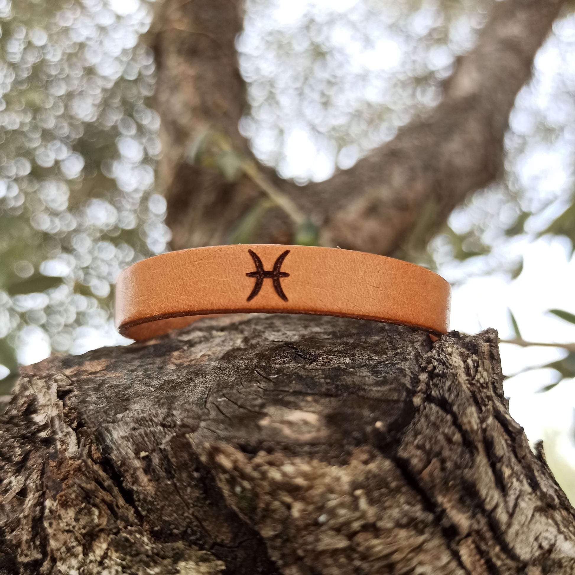 A brown leather bracelet with pisces´ symbol engraved on it.